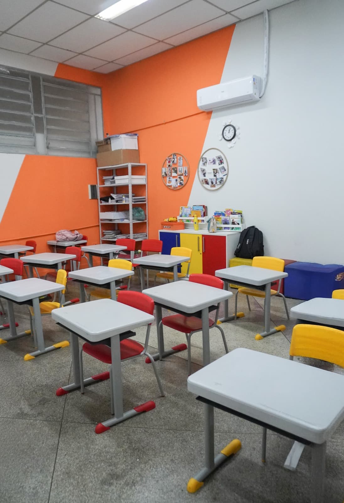 Sala com mesas brancas e cadeiras vermelhas e amarelas
